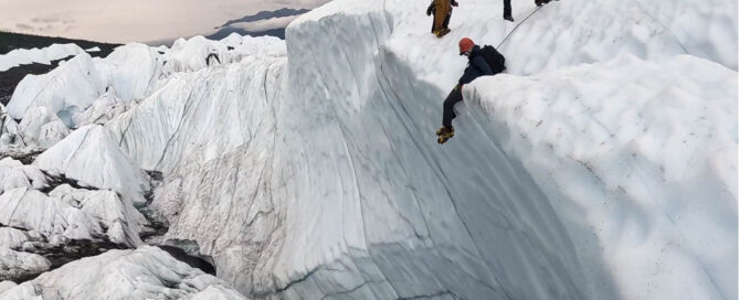 climbers and ropes on glacier ice fin above chasm