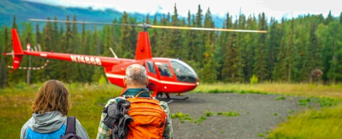 people with backpacks on facing red helicopter in distance