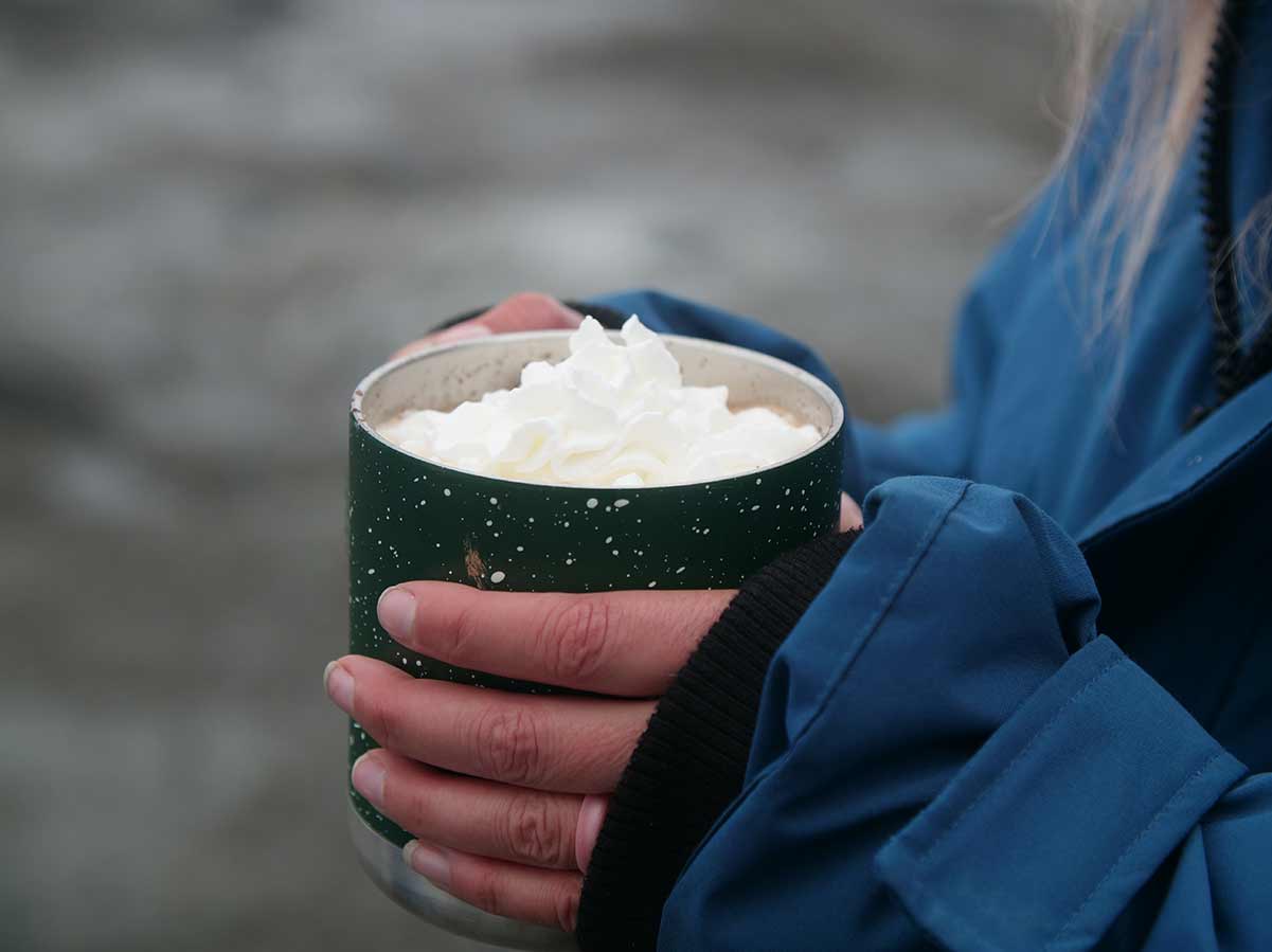 glaciercamphotcocoa person holding hot cocoa in a green mug with cream