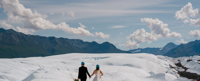 two people walking on a glacier with wedding attire on with Alaska scenery in background
