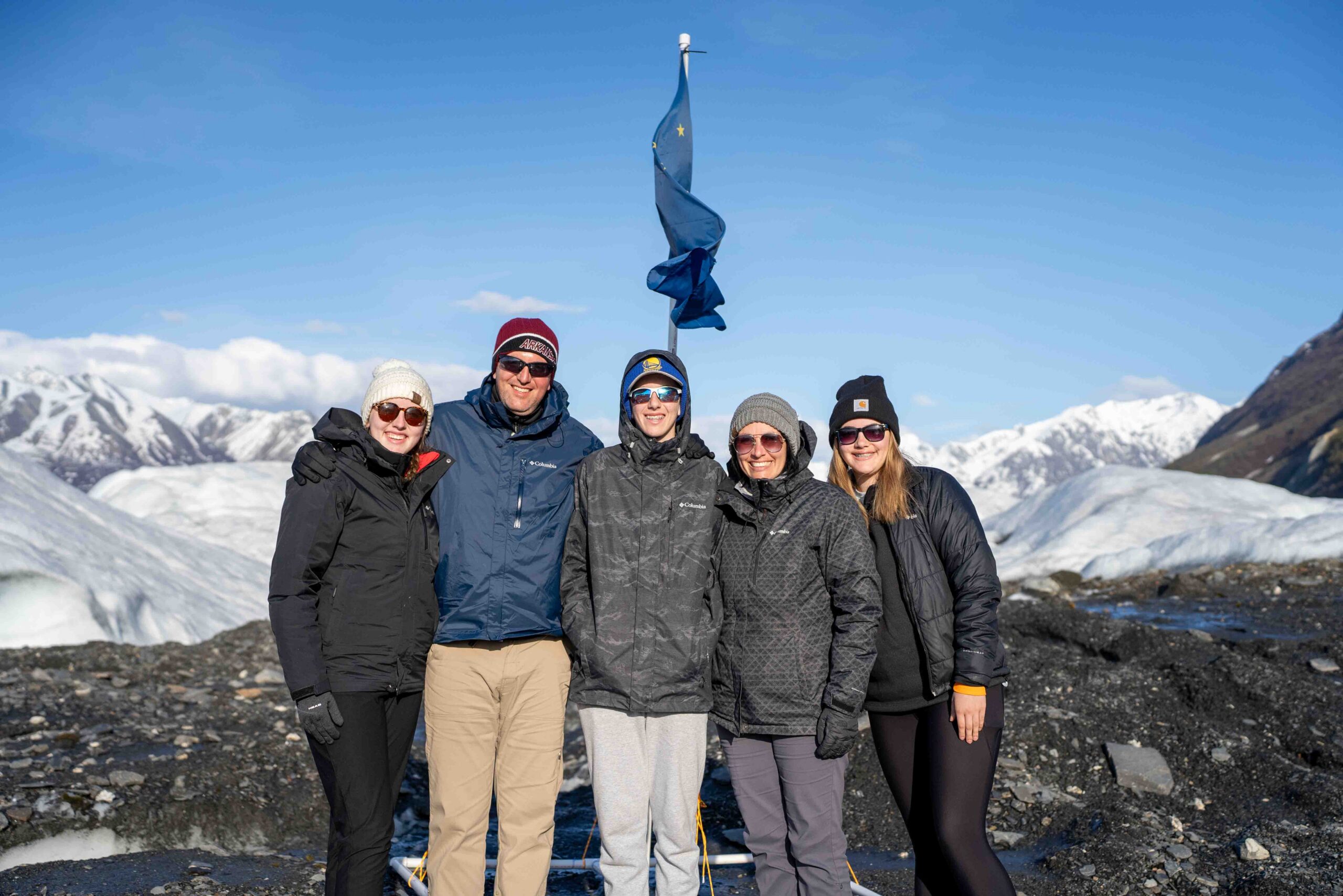 family stands in front of the Alaska flag at glacier camp