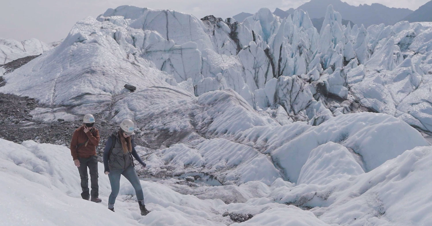 two people walk near the glacier ice fall