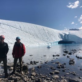 Two people standing in front of a blue glacial pool