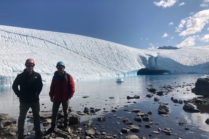Two people standing in front of a blue glacial pool