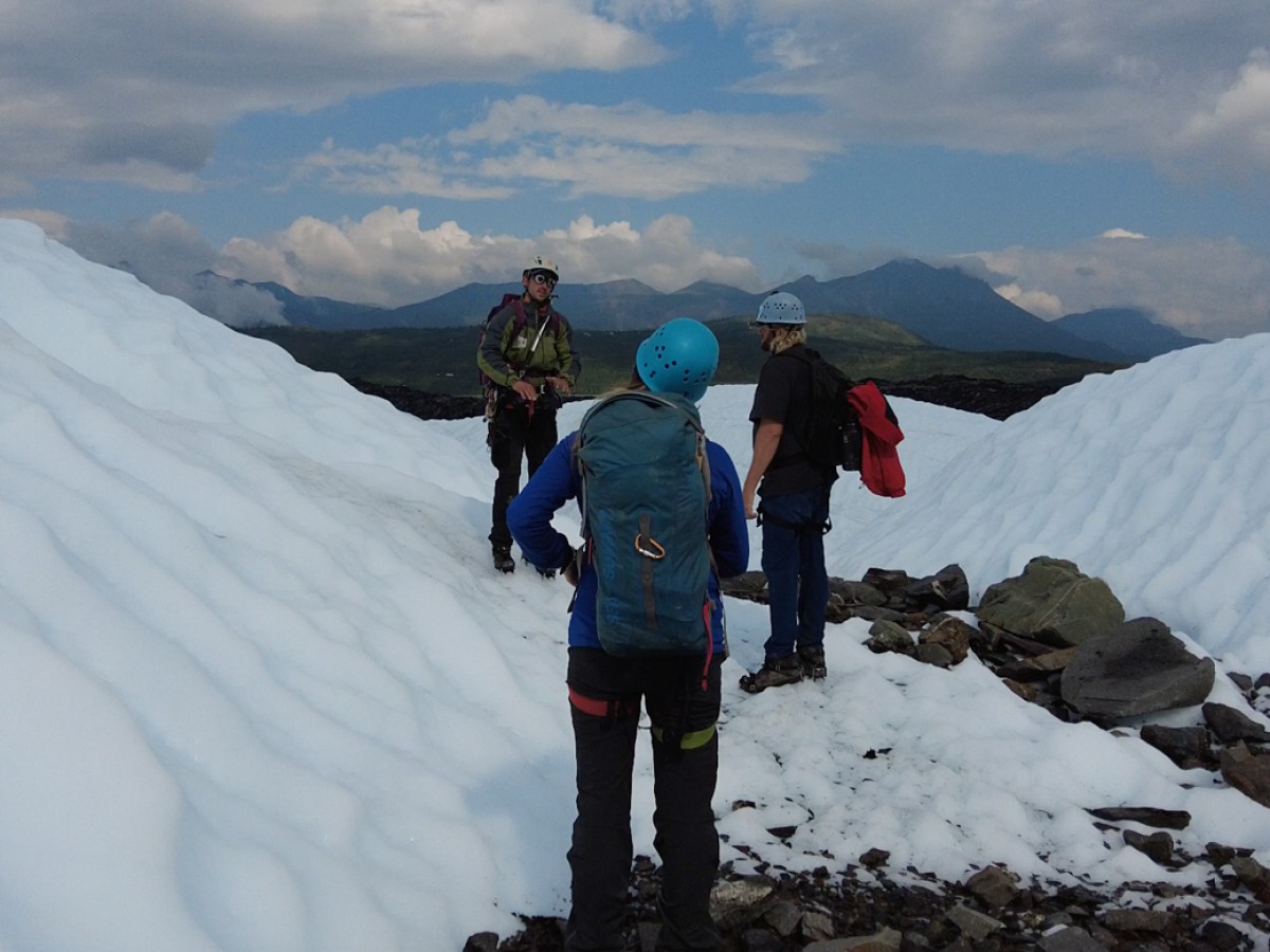 three people wearing helmets talk near boulders and white ice