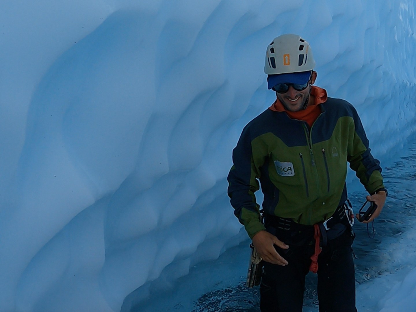 man standing in blue ice canyon on glacier