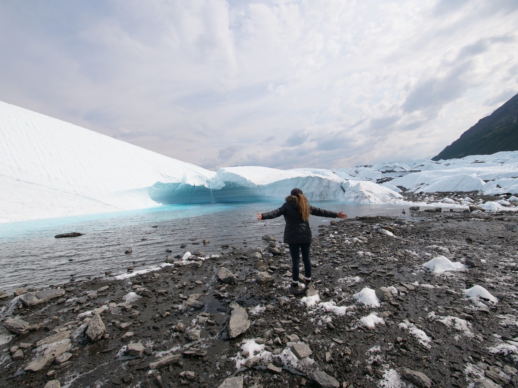 lady standing with arms open in front of blue ice waterfall