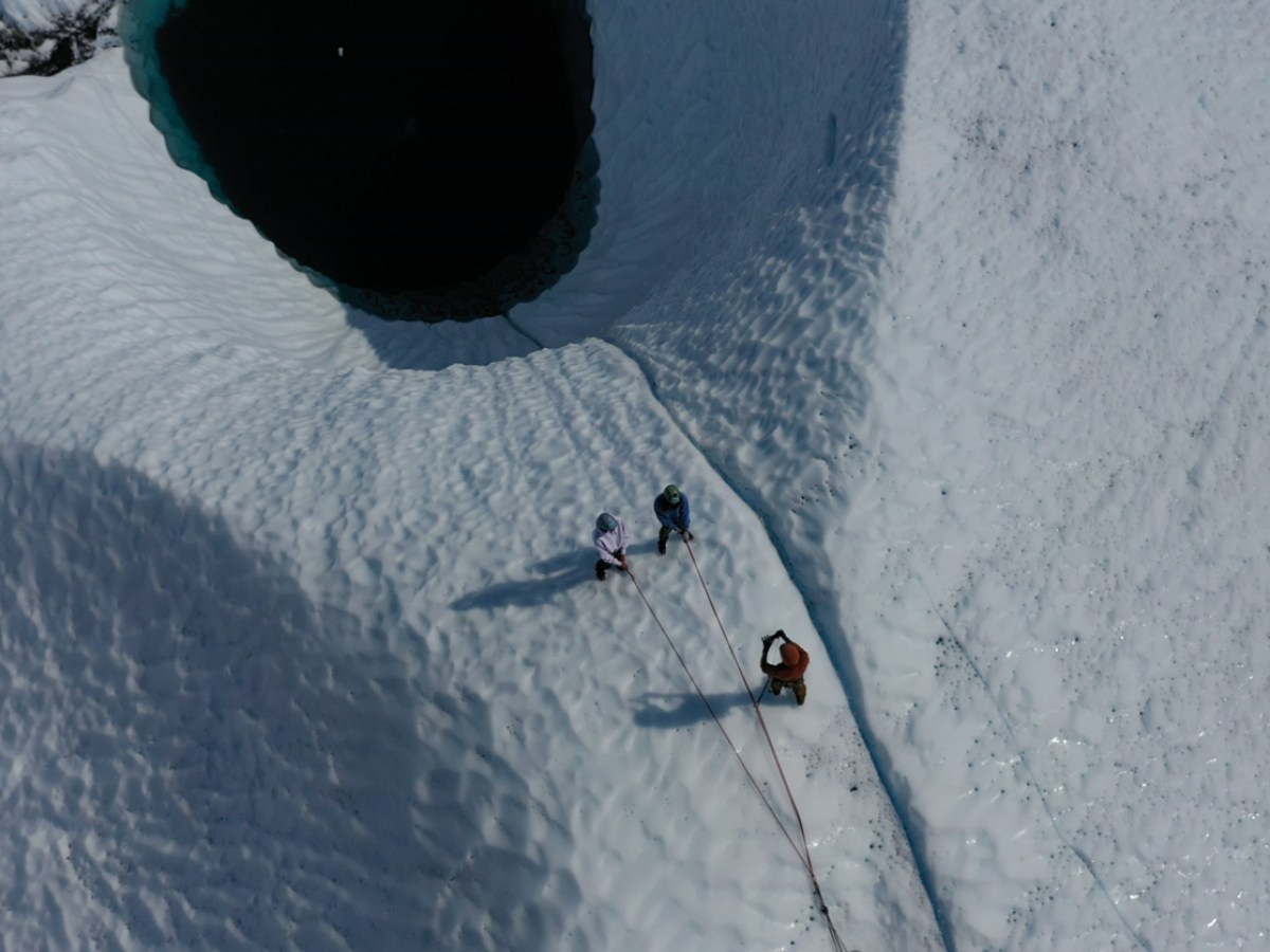 people hanging over a blue glacier pool