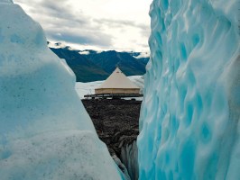 view from blue ice cavern to look at canvas tent on moraine with mountains in background
