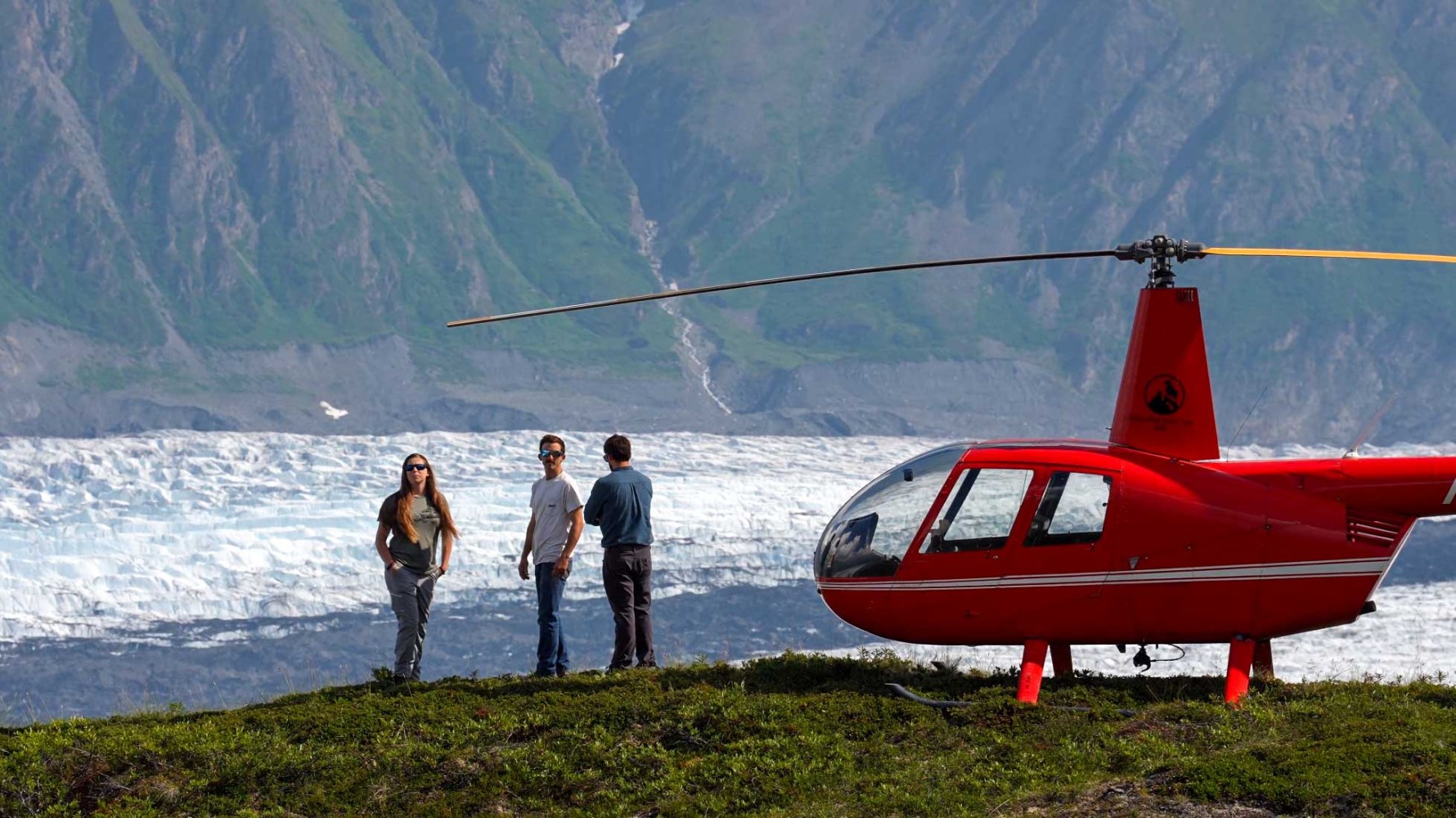 three people overlooking glacier standing next to red helicopter