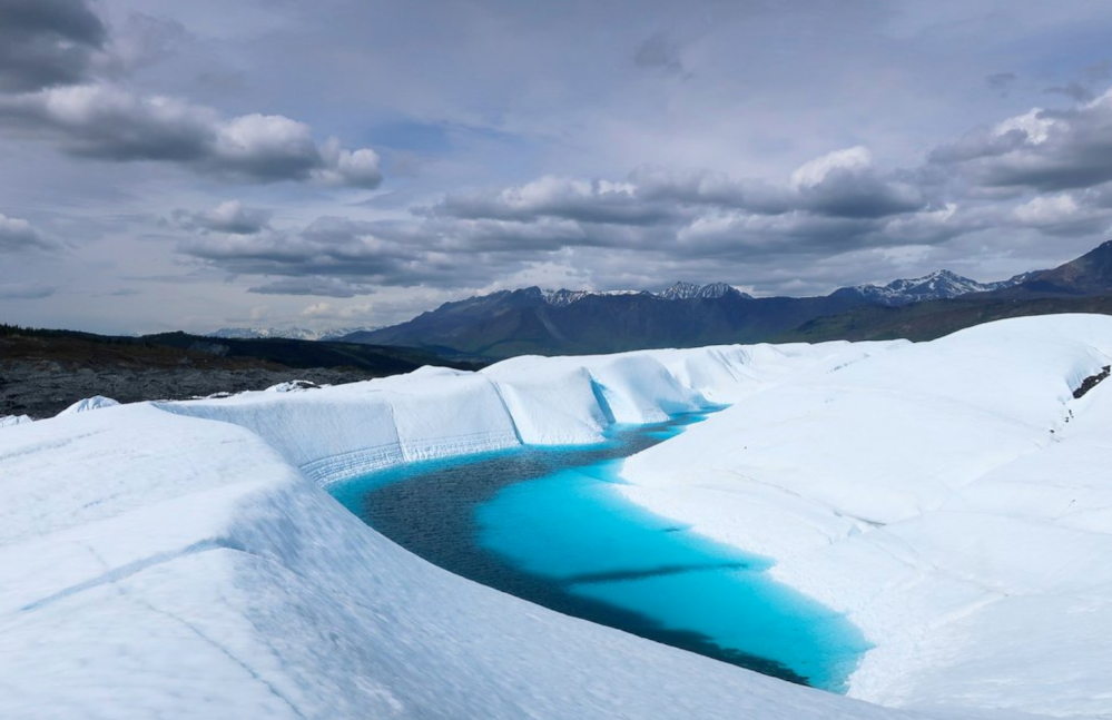 blue glacier meltwater on white ice with mountains and clouds in the background